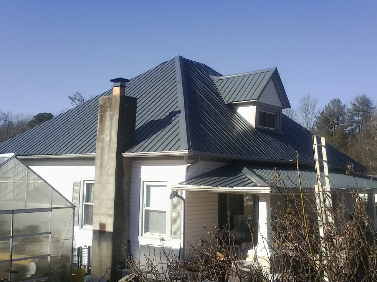 Dark blue standing seam metal roof on a white farmhouse with dormer — Slate & Tile Roof Repair by Roofing Brothers in Metz