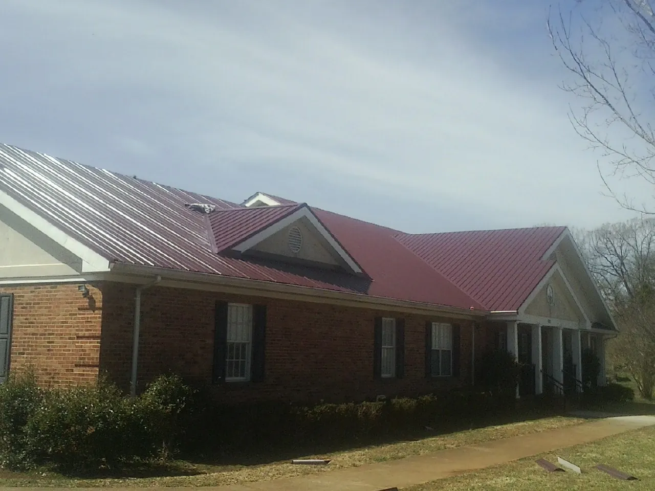 Red metal roof with gabled entries on a long brick building, from a Hail Damage Roof Repair job in Metz