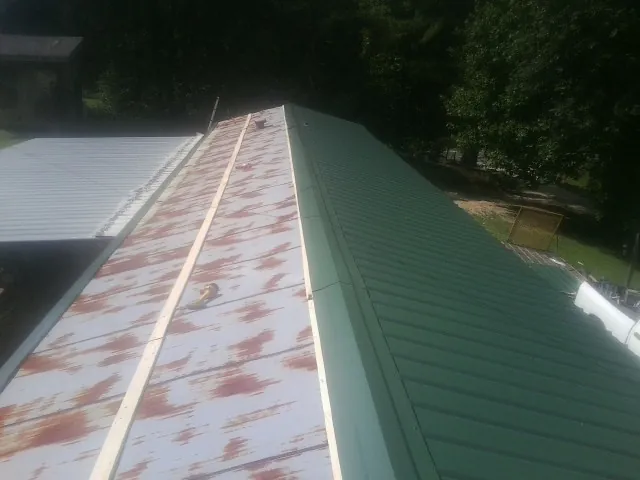 Old rusted panels beside newly installed green metal roofing — Wind Damage Roof Repair by Roofing Brothers in Metz