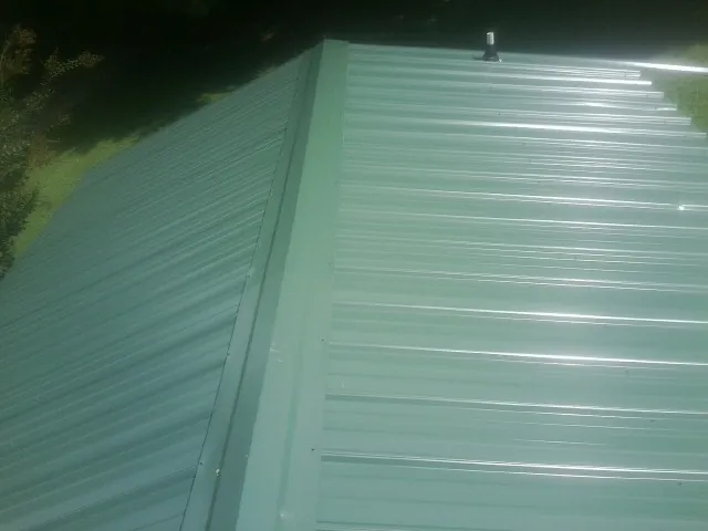 New green metal panels meeting at the ridge of a roof — Flat Roof Repair work by our crew in Metz