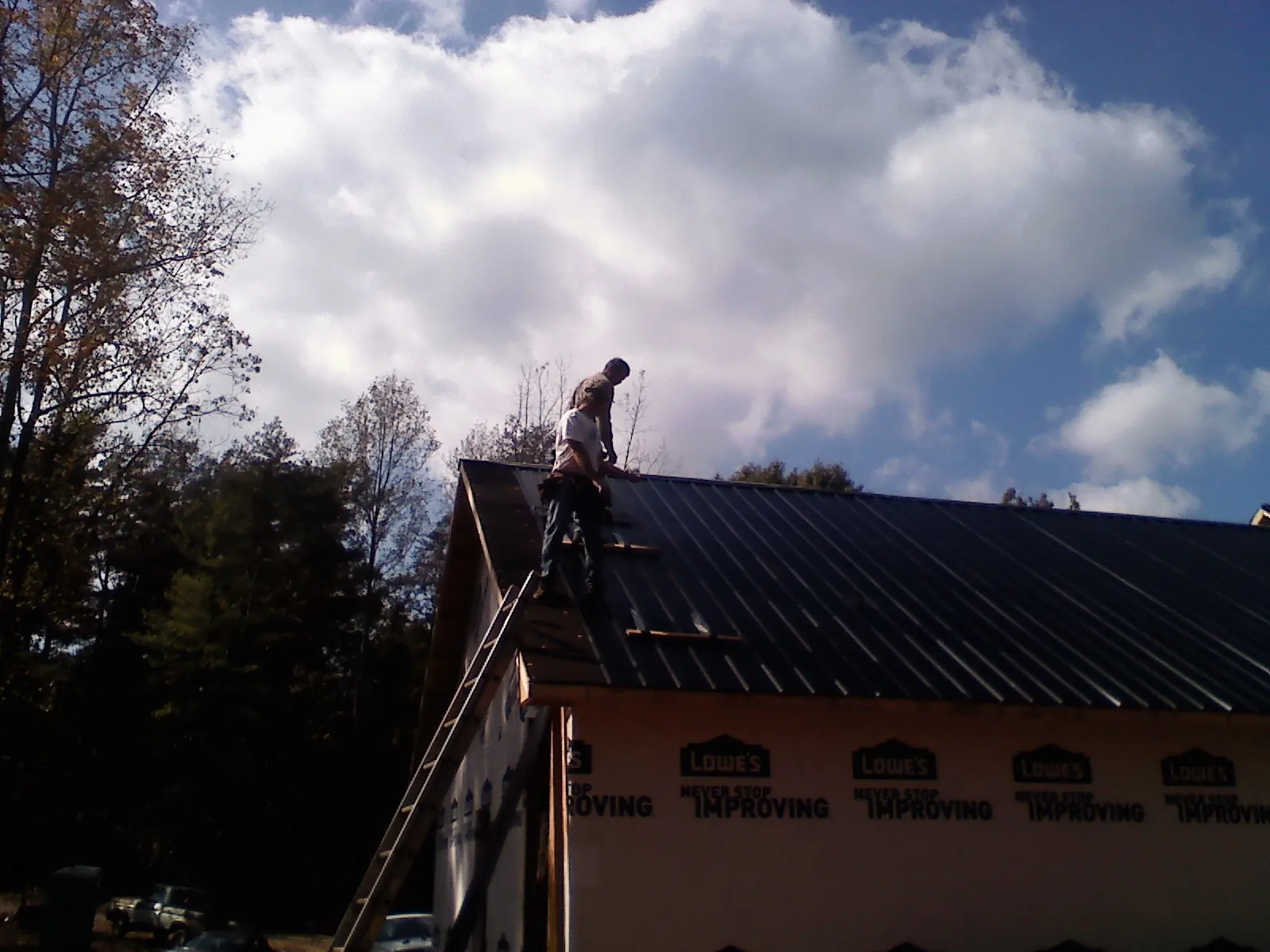 Roofer fastening dark metal panels high against a cloudy sky, from a Roof Inspection job in Metz