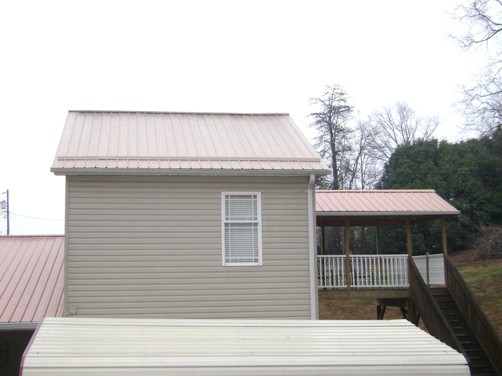 Tan metal roofs on a two story addition and attached porch, from a Roof Replacement job in Metz